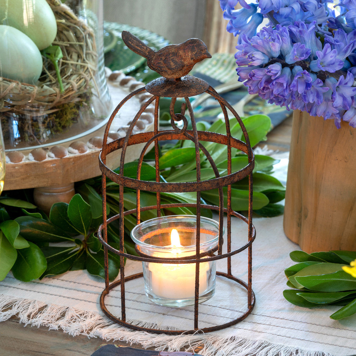 vintage birdcage votive on table top with purple flowers candle and eggs