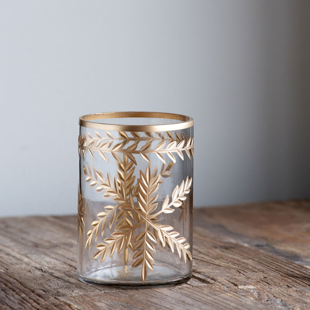 clear glass empty hurricane vase etched with gold on a wood table