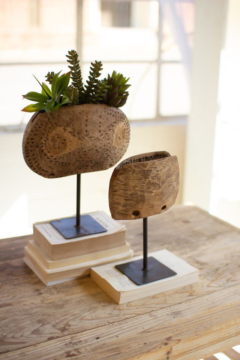 two wood cow bell planters on stands stacked on books on a table