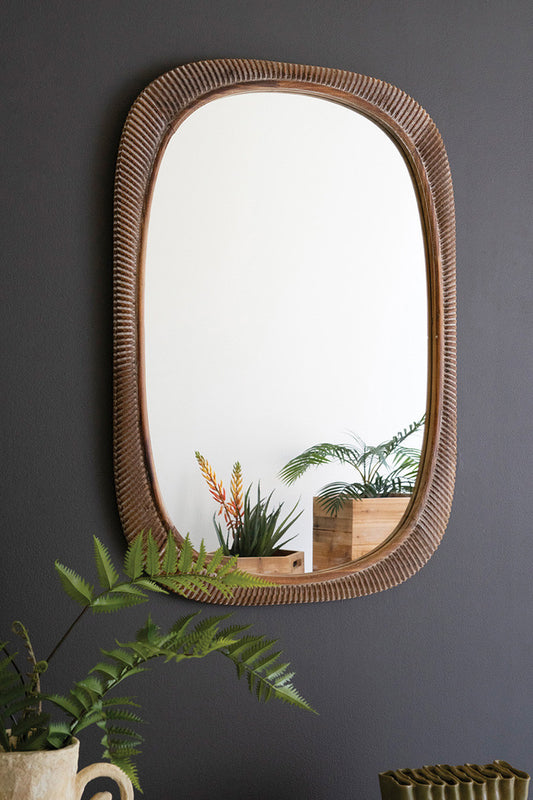unique shaped wood mirror on a gray wall with faux plants styled in front