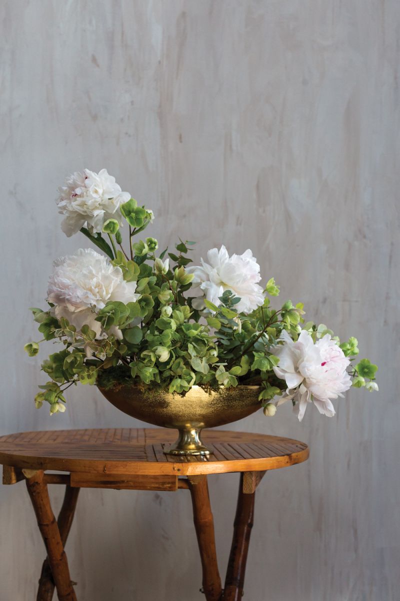 white peonies with green helebores in a white oblong footed vase on a wood table
