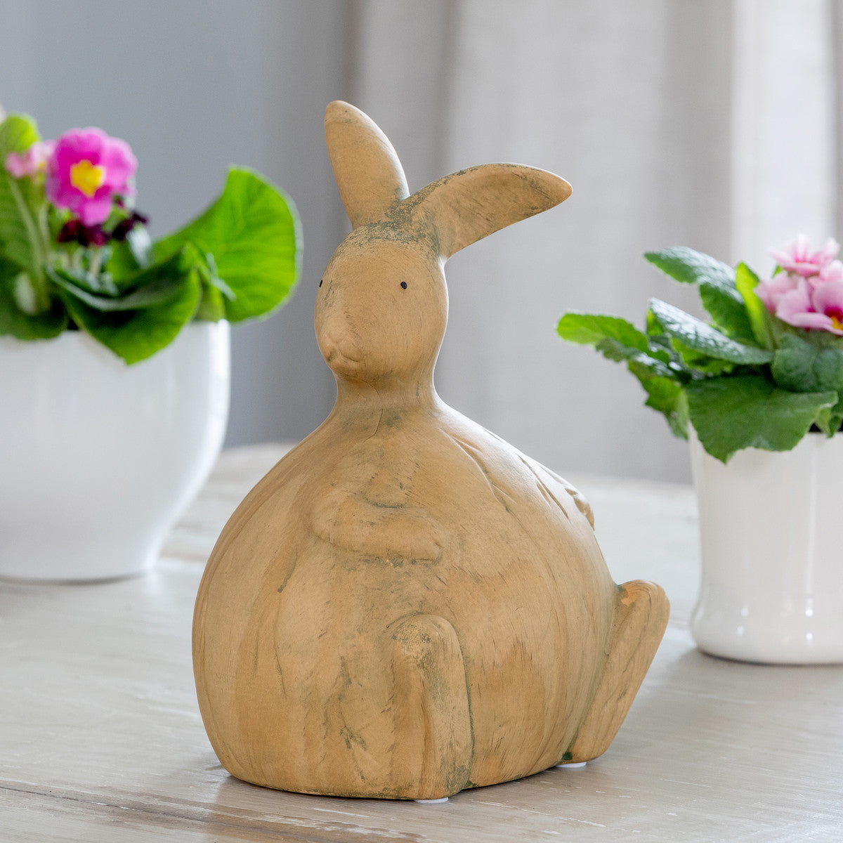 whimsical wood bunny rabbit on table with african violet real and faux flowers in white pots