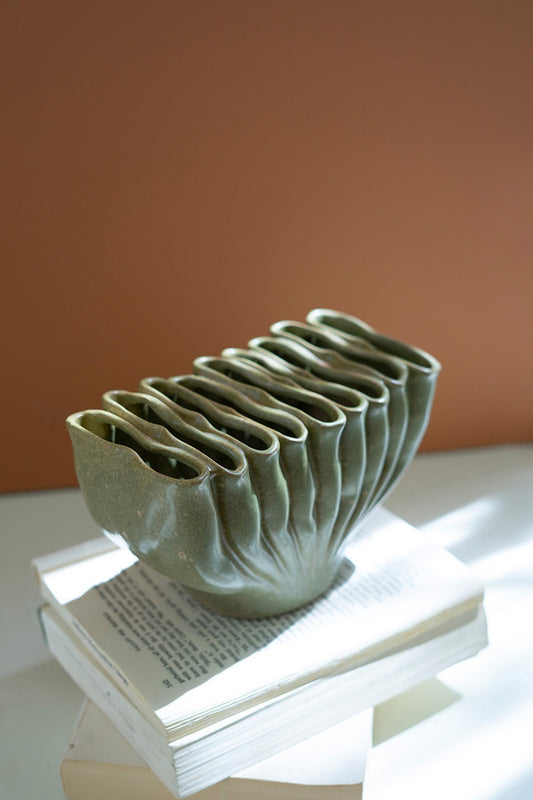 green ceramic vase with folds on a stack of books