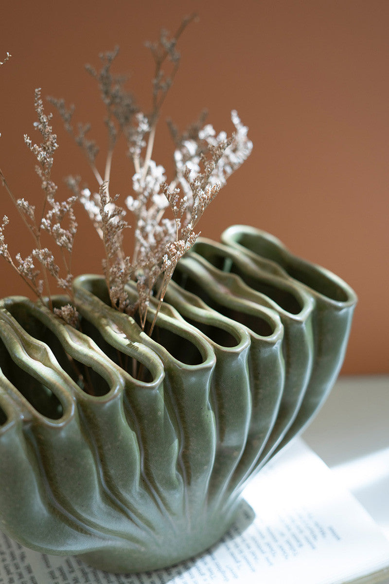 green ceramic vase with folds and minimal floral fronds on a stack of books