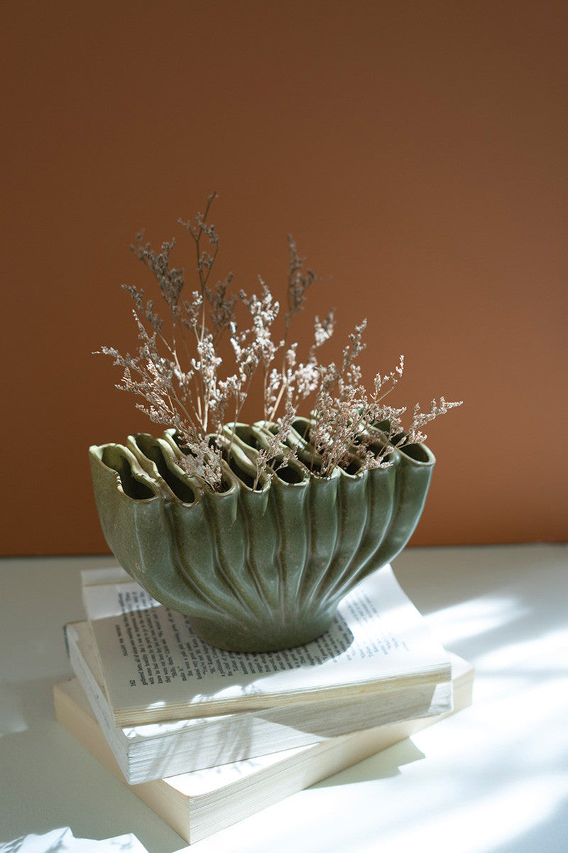 green ceramic vase with modest botanicals on a stack of books in front of an orange wall