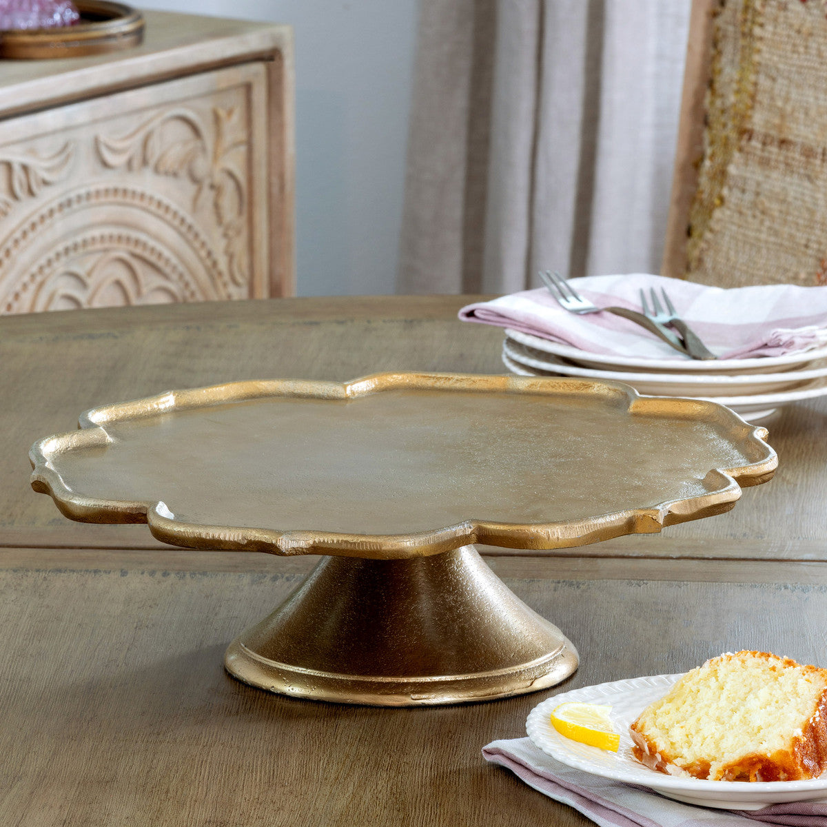 scalloped edge cast aluminum neutral gold cake stand on a kitchen table next to a slice of pound cake