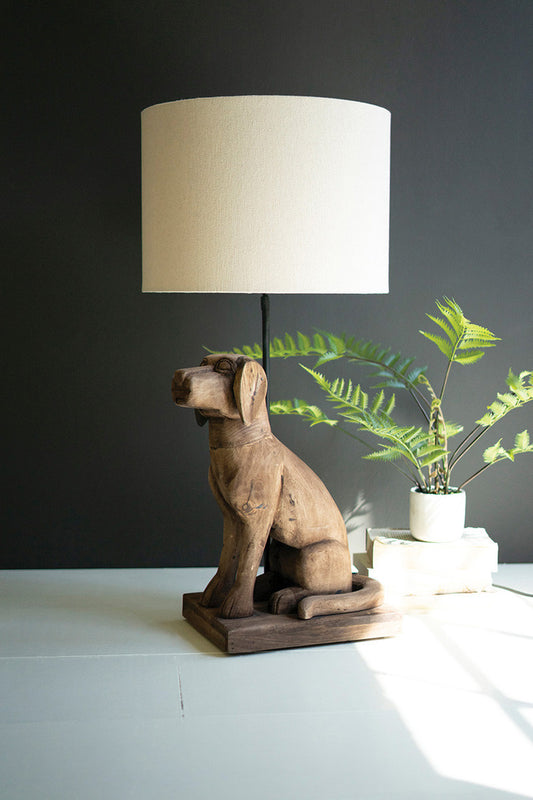whimsical wood dog table lamp with a linen shade on a table with a  fern plant in the background