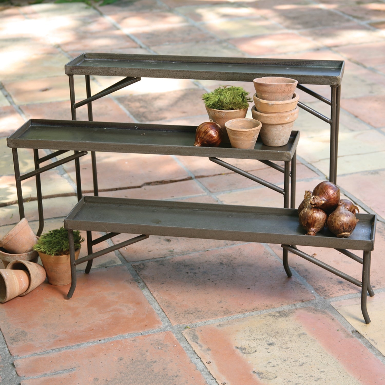 three forged iron racks on a patio styled with terra-cotta pots, plants, moss and onions