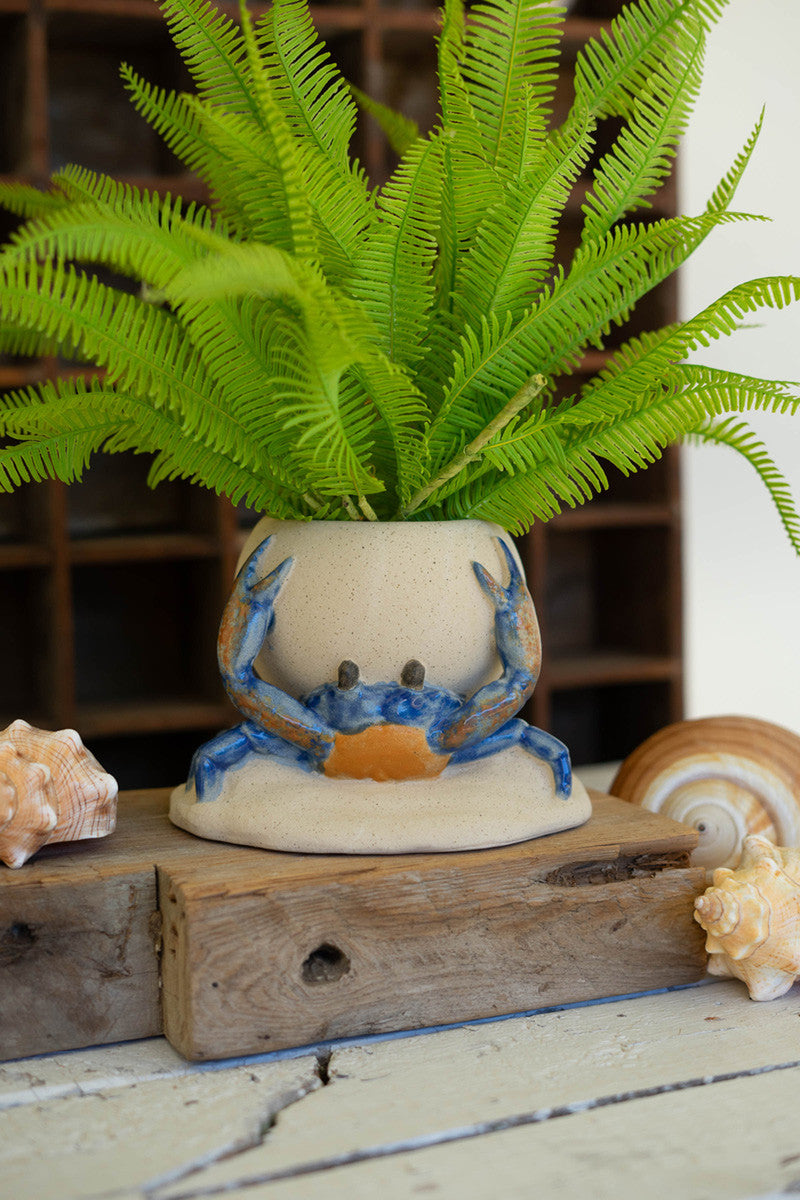 A blue and orange crab planter with a artificial fern on a wood riser