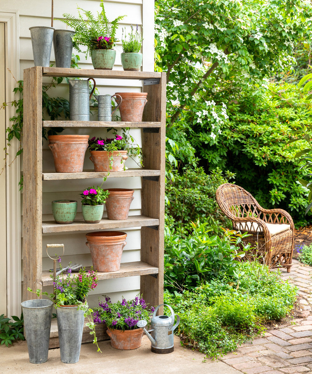 wood potter shelf with metal gardener cans and terra cotta plant pots in garden  patio 