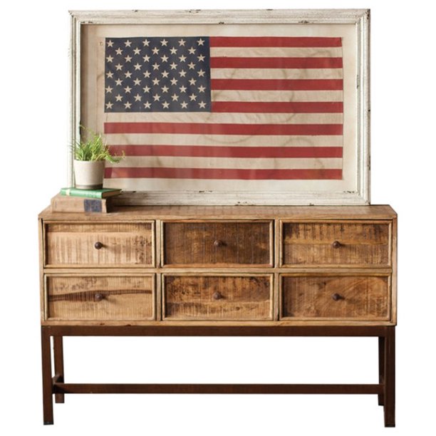 framed american flag under glass  on a wood cabinet with a faux plant