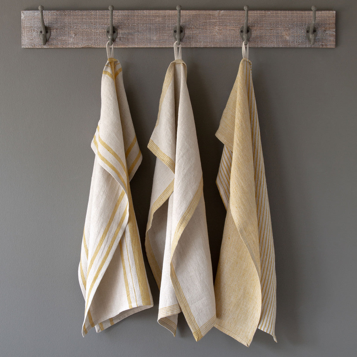 three soft linen yellow dish towels hanging on rustic rack