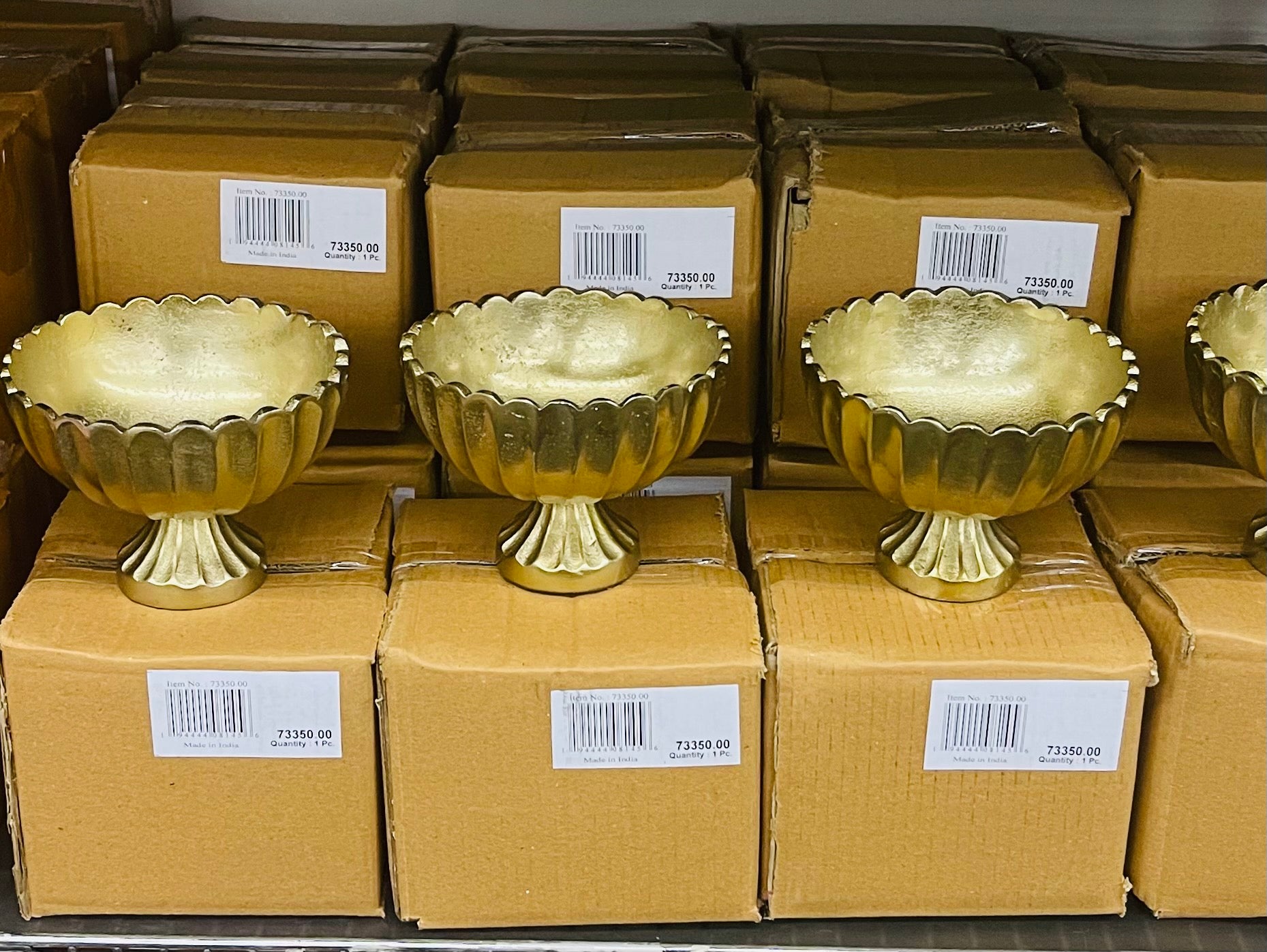 gold scallop edge compote vases lined up in shop with cardboard boxes